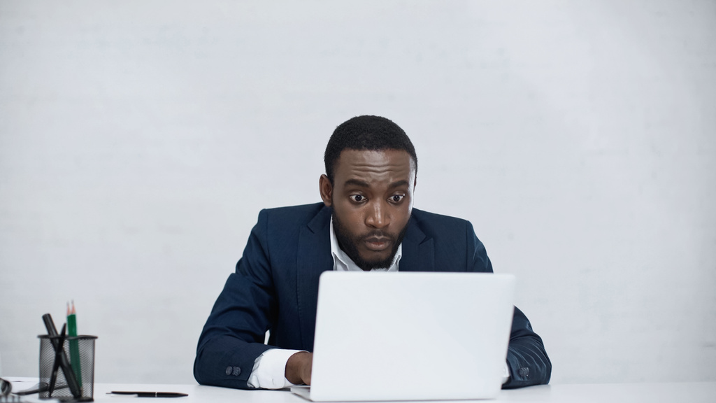 choqué homme d'affaires afro-américain utilisant un ordinateur portable isolé sur gris  - Photo, image
