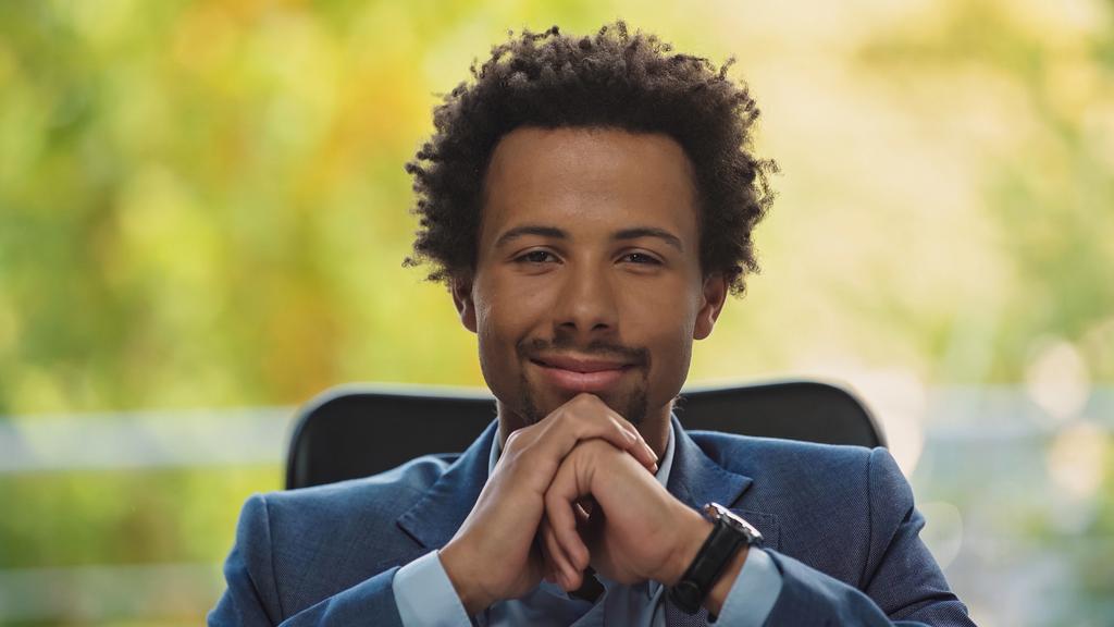 giovane e affermato uomo d'affari africano americano sorridente alla telecamera in ufficio - Foto, immagini