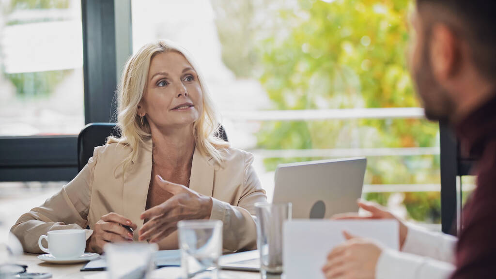 бізнес-леді середнього віку вказує з рукою, розмовляючи з розмитими менеджерами в офісі
 - Фото, зображення