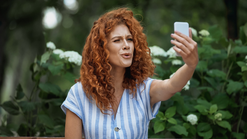 Lockige rothaarige Frau macht Selfie im grünen Park  - Foto, Bild