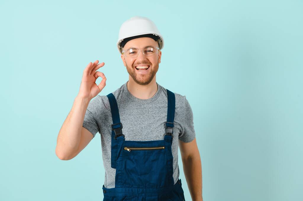 Τεχνίτες ή ηλεκτρολόγος άνθρωπος πάνω από απομονωμένο μπλε φόντο δείχνει μια πινακίδα ok με τα δάχτυλα - Φωτογραφία, εικόνα