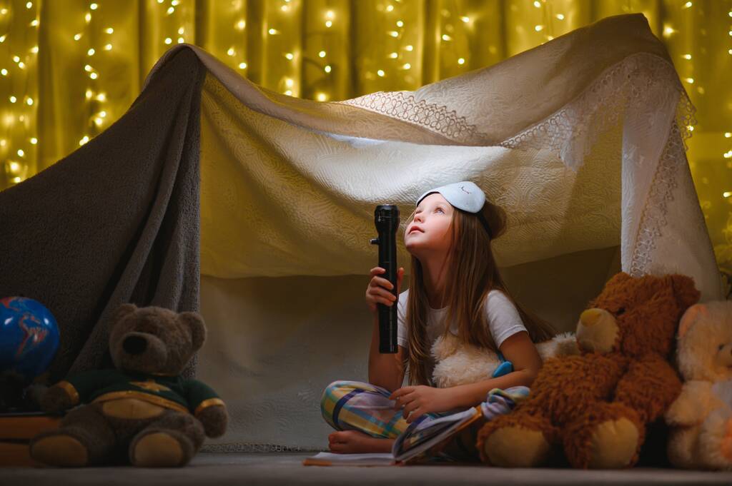 child girl reading with book and flashlight and teddy bear in tent. before going to bed - Photo, Image