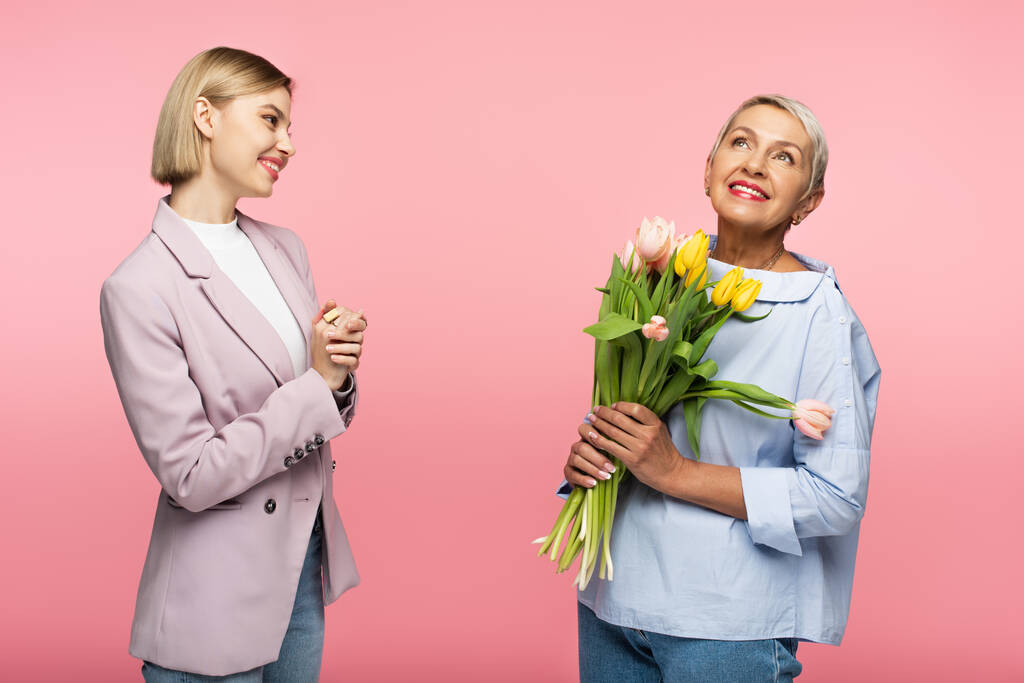 felice madre di mezza età che tiene mazzo di fiori vicino a figlia soddisfatta isolato su rosa  - Foto, immagini