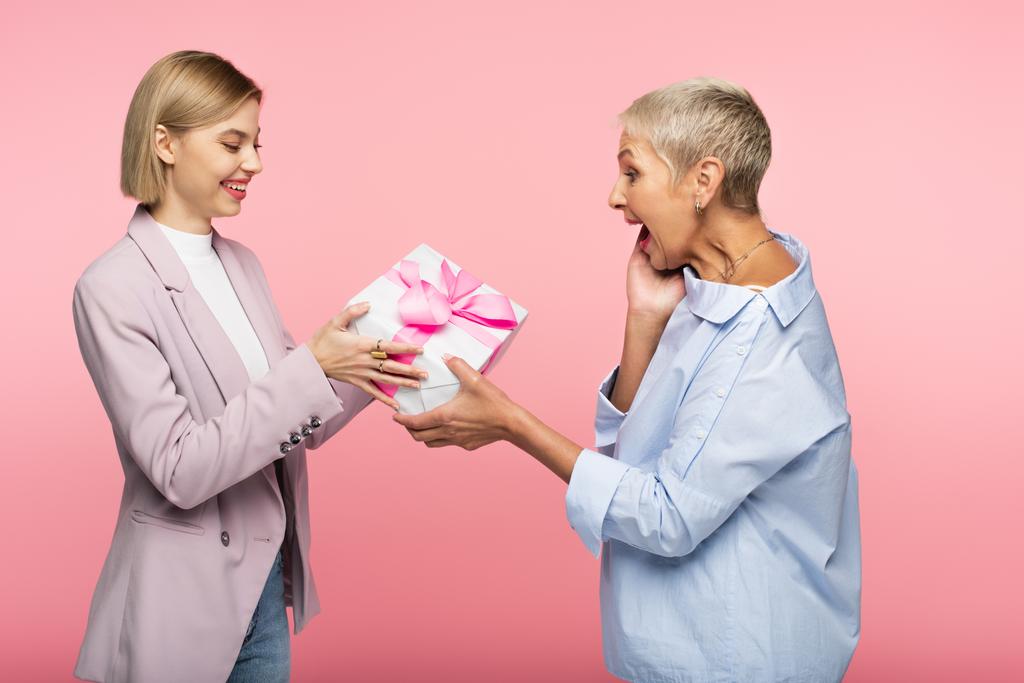 gelukkig vrouw geven verpakt cadeau naar opgewonden volwassen moeder geïsoleerd op roze - Foto, afbeelding