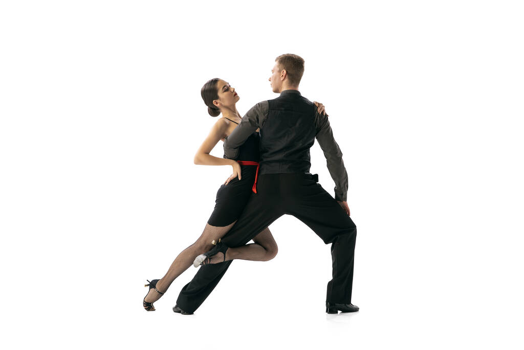 Prachtige sportieve jonge man en vrouw dansen Argentijnse tango geïsoleerd op witte studio achtergrond. Kunstenaars in zwarte kostuums - Foto, afbeelding