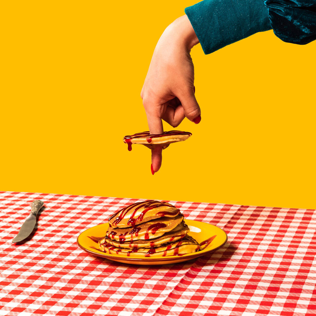Φωτογραφία από ποπ τέχνη φαγητού. Γυναικεία χέρια και γλυκές τηγανίτες σε καρό τραπεζομάντηλο που απομονώνονται σε φωτεινό κίτρινο φόντο. Εσοδεία, ρετρό στυλ - Φωτογραφία, εικόνα