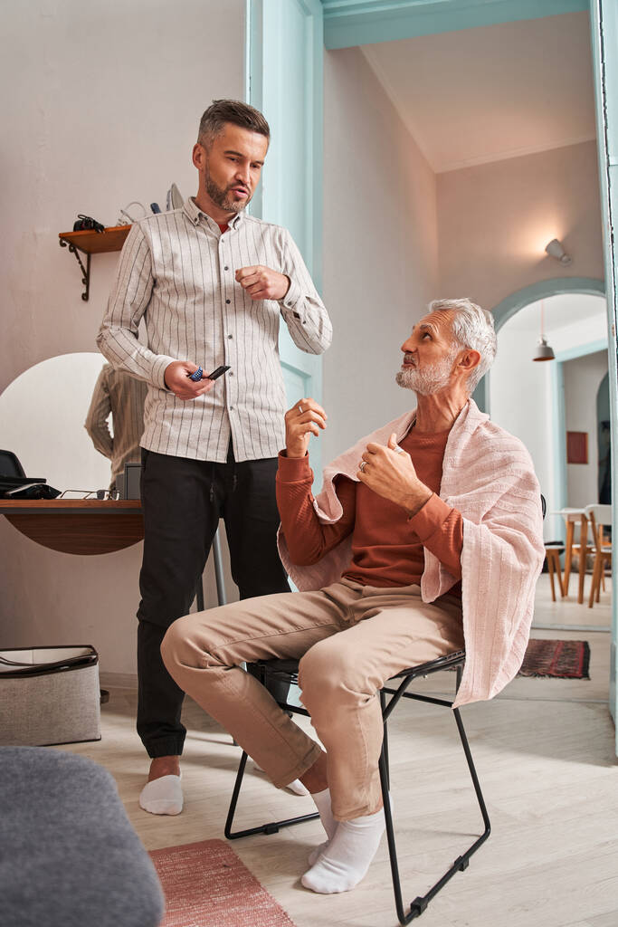 El padre jubilado y su hijo adulto discuten nuevo corte de pelo mientras pasan tiempo en casa - Foto, Imagen