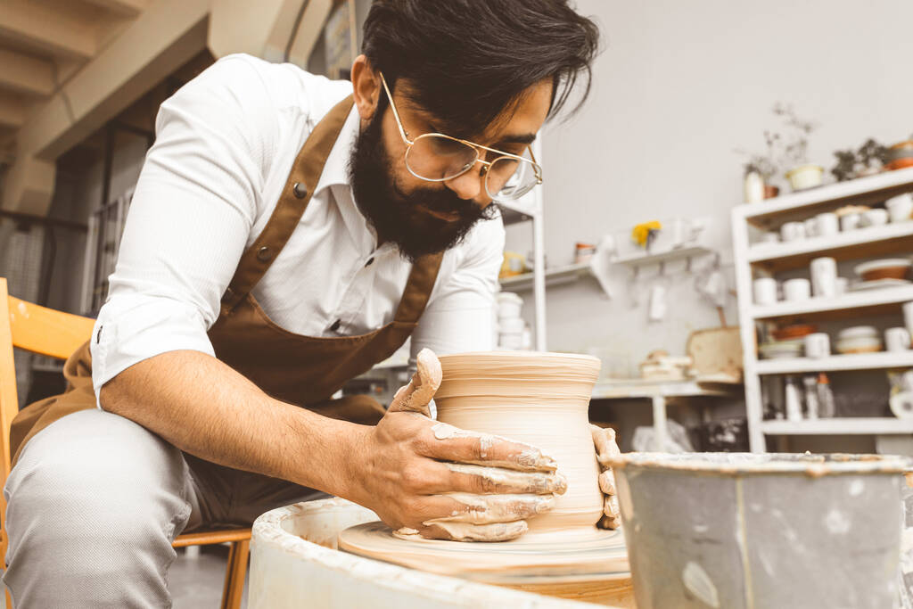 Un jeune potier masculin est engagé dans l'artisanat dans son atelier sur une roue de potiers et fabrique un produit en argile - Photo, image