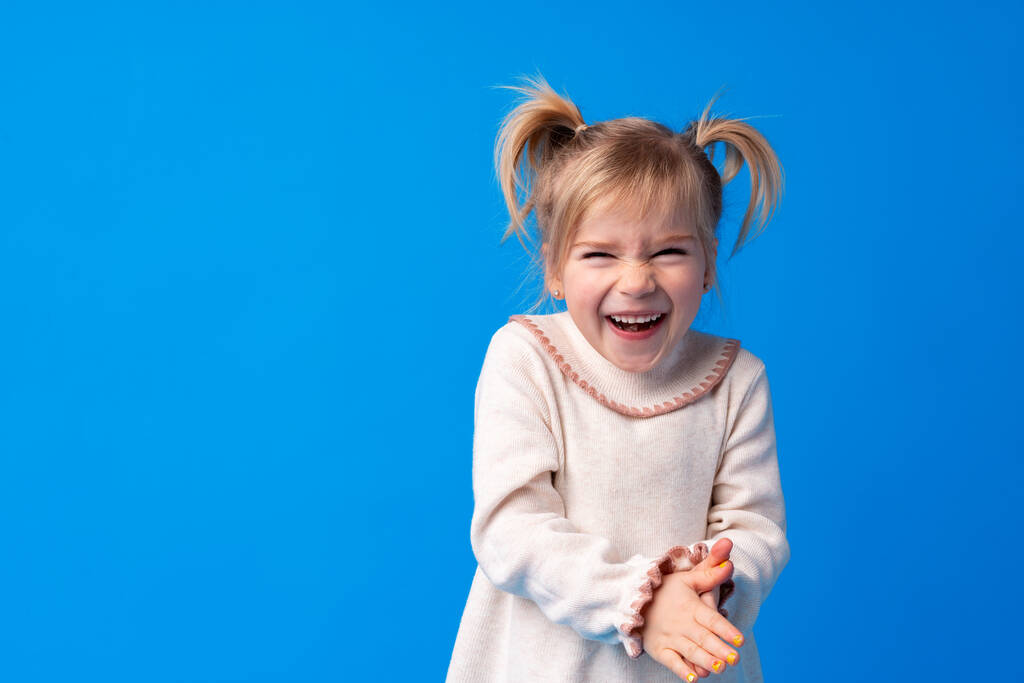 Fröhlich charmantes kleines Mädchen lächelt und lacht vor blauem Hintergrund - Foto, Bild