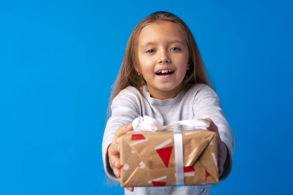 Šťastná holčička s dlouhými vlasy drží dárkovou krabici na modrém pozadí - Fotografie, Obrázek