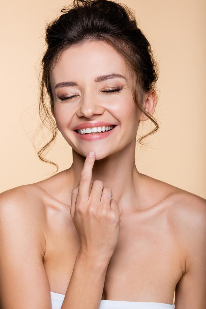 Happy brunette woman touching chin isolated on beige  - Photo, Image