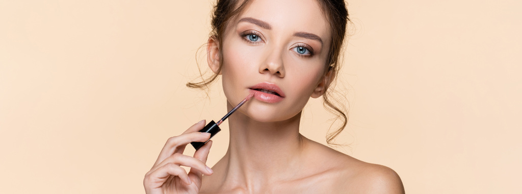 Pretty young model applying lip gloss isolated on beige, banner  - Photo, Image