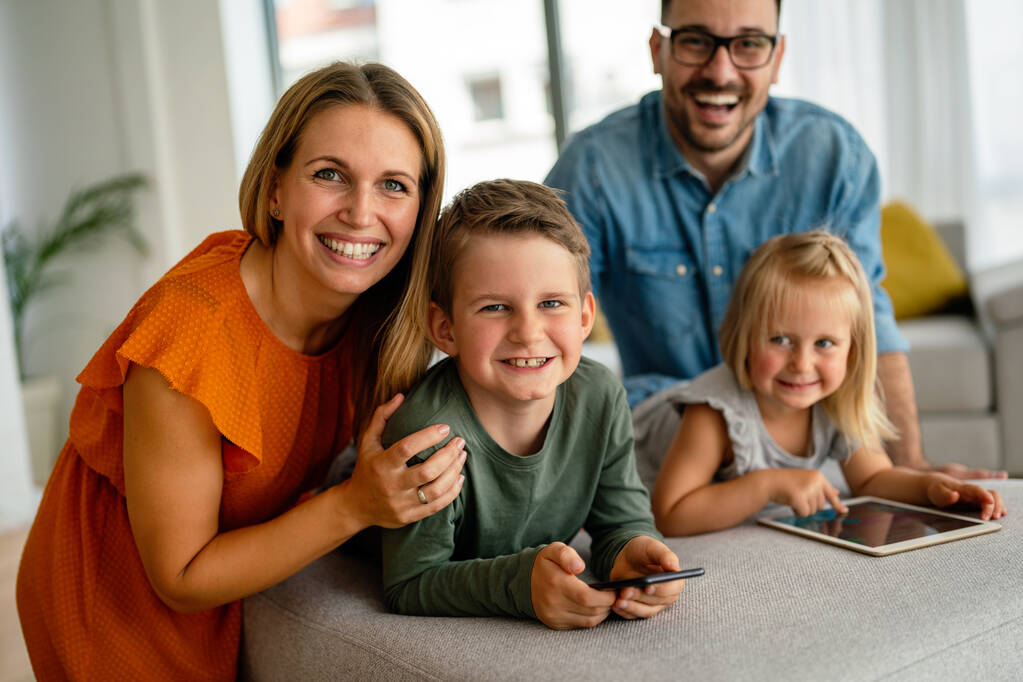 Onnellinen nuori perhe pitää hauskaa kotona. Vanhemmat, joiden lapset käyttävät digitaalista laitetta. Koulutus vanhemmuus onnellisuus käsite. - Valokuva, kuva