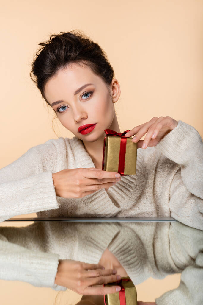 Stylish woman in sweater holding present near mirror isolated on beige  - Photo, Image