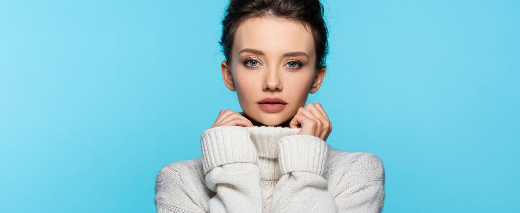 Brunette model in sweater looking at camera isolated on blue, banner  - Photo, Image