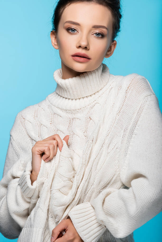 Model looking at camera while touching sweater isolated on blue - Photo, Image