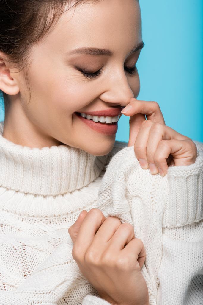 Retrato de mujer sonriente en suéter acogedor cerrando los ojos aislados en azul - Foto, imagen
