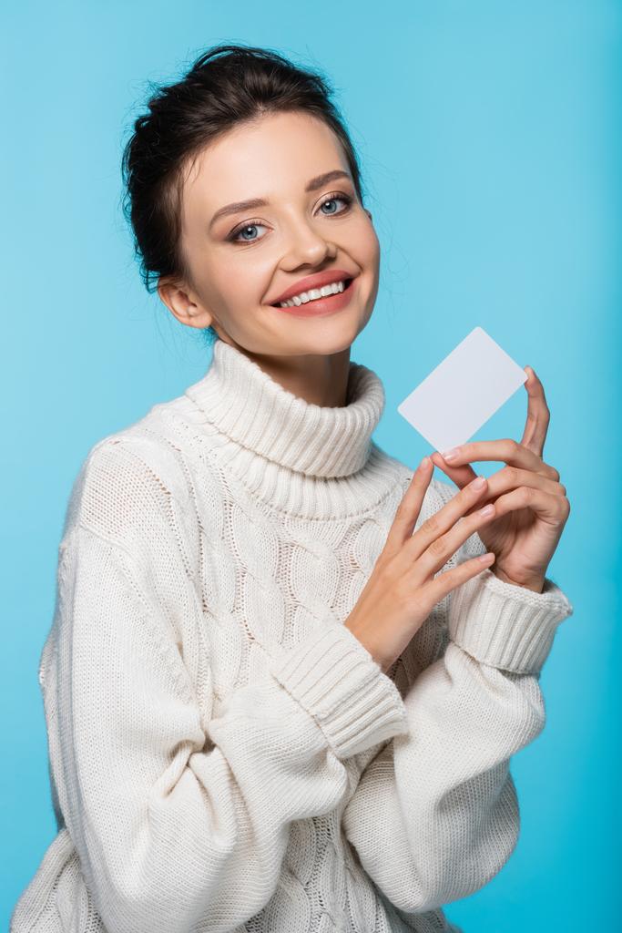 Mulher alegre em camisola de malha branca segurando cartão em branco isolado no azul - Foto, Imagem