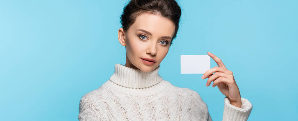 Μελαχρινή μοντέλο σε πλεκτό πουλόβερ κρατώντας λευκή κάρτα απομονώνονται σε μπλε, banner  - Φωτογραφία, εικόνα