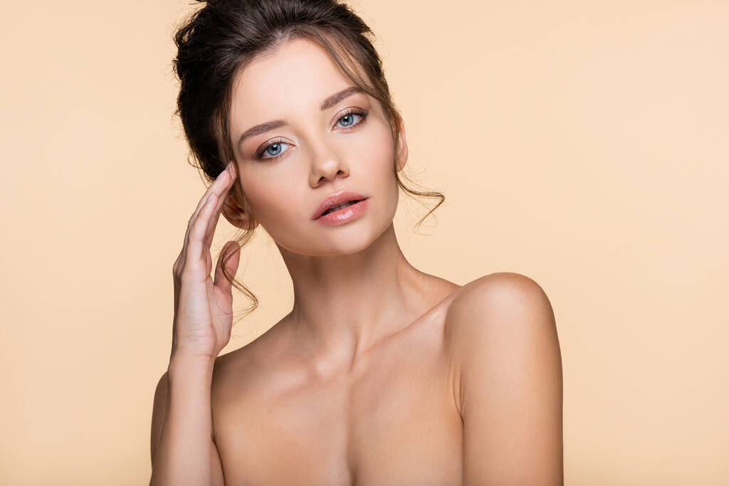 Brunette woman with naked shoulders looking at camera isolated on beige  - Photo, Image