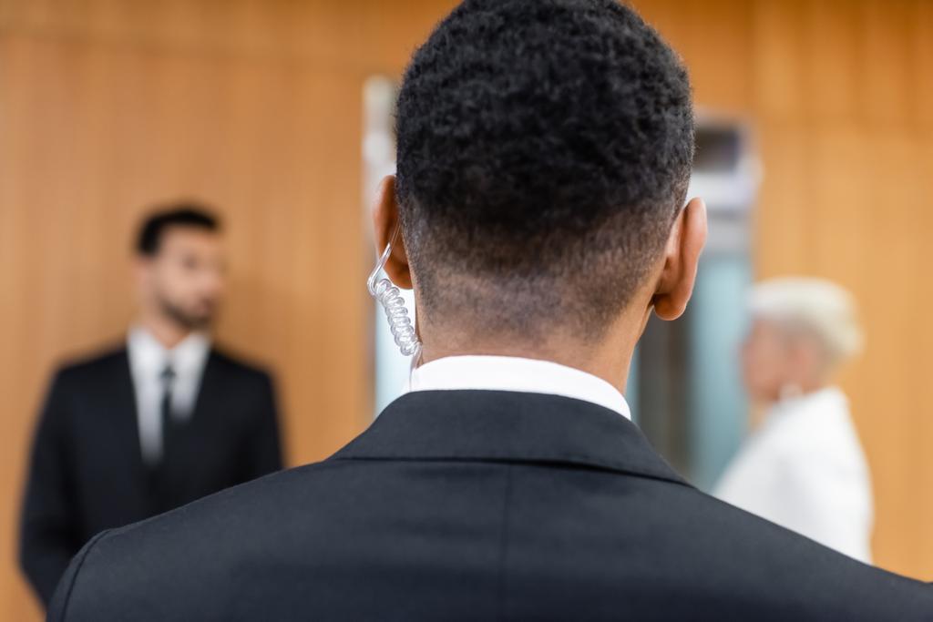 visão traseira do homem de segurança afro-americano perto de mulher sênior borrada com guarda-costas em fundo borrado - Foto, Imagem