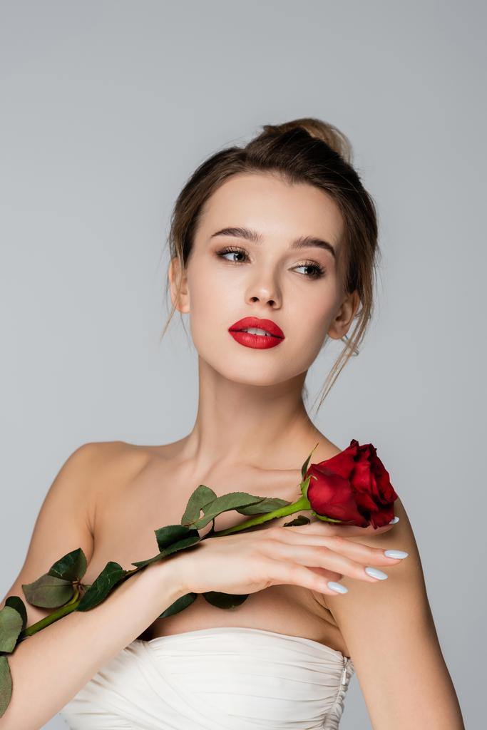 sensual young woman in strapless top posing with red rose isolated on grey - Photo, Image