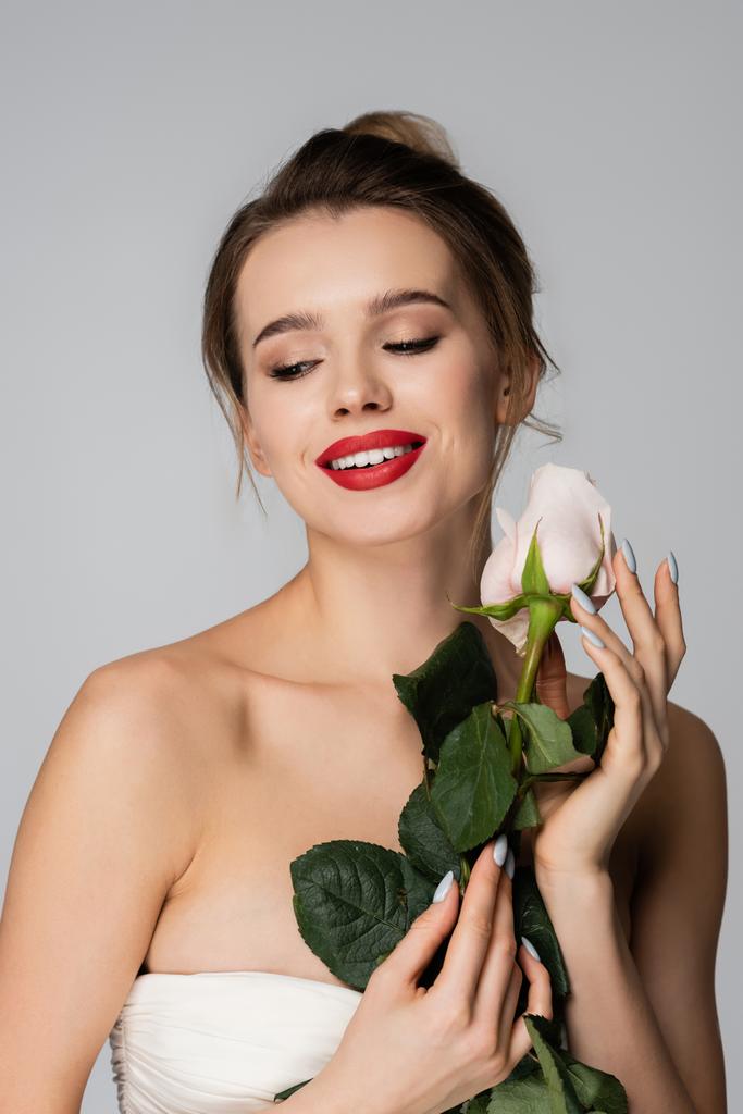 uśmiechnięta kobieta z gołymi ramionami trzymająca białą różę na szarym - Zdjęcie, obraz