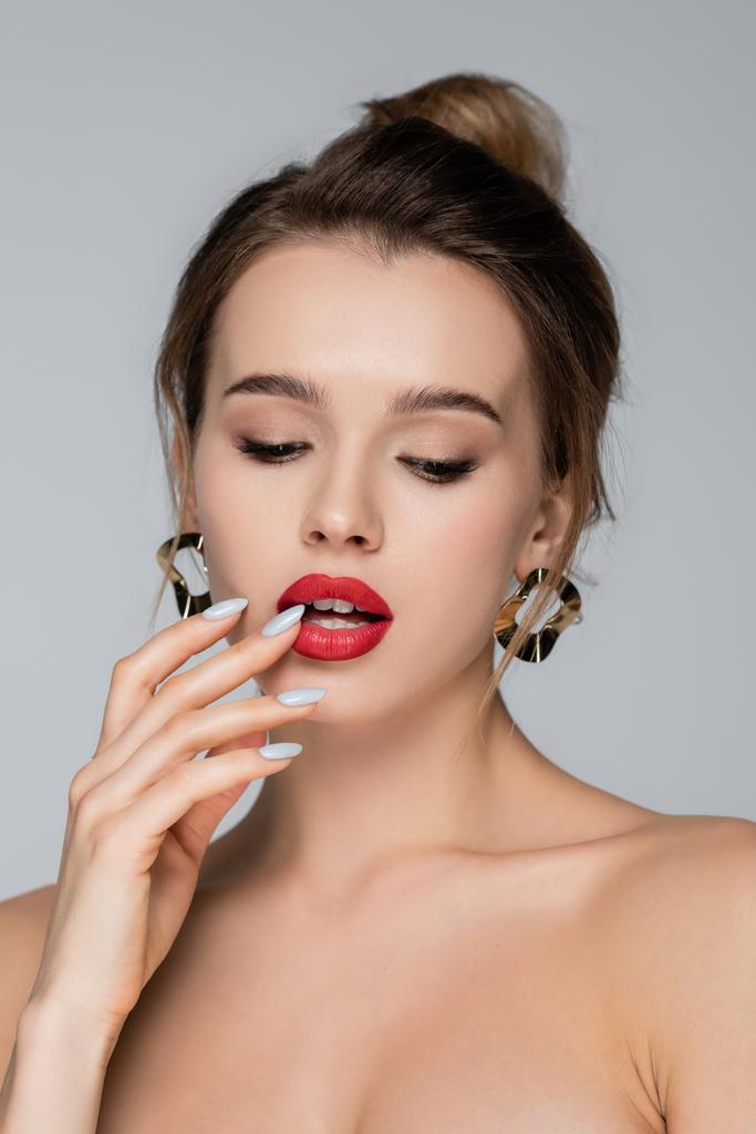 mujer sensual con maquillaje tocando los labios rojos aislados en gris - Foto, Imagen