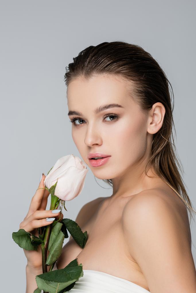 γοητευτική γυναίκα με τέλειο δέρμα κρατώντας λευκό τριαντάφυλλο απομονώνονται σε γκρι - Φωτογραφία, εικόνα