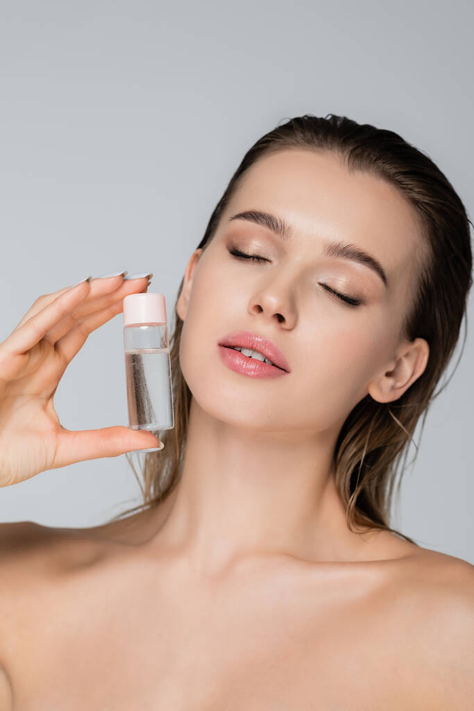 young woman with perfect skin and closed eyes holding cosmetic oil isolated on grey - Photo, Image