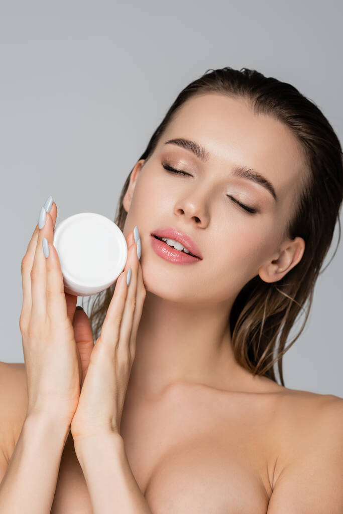 young woman with wet hair and closed eyes holding cosmetic cream isolated on grey - Photo, Image