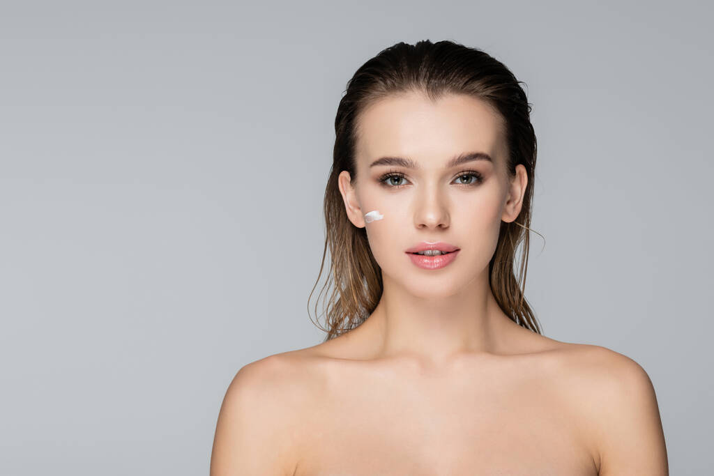 charming woman with wet hair, naked shoulders and cosmetic cream on face isolated on grey - Photo, Image