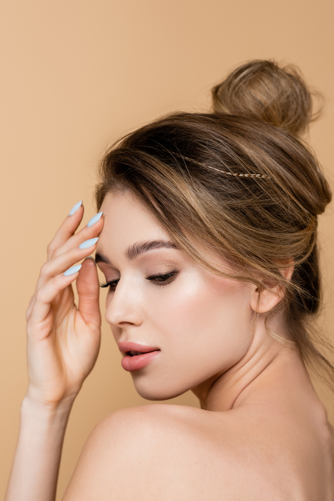 mladá žena s přirozeným make-up a holé rameno dotýkat čelo izolované na béžové - Fotografie, Obrázek