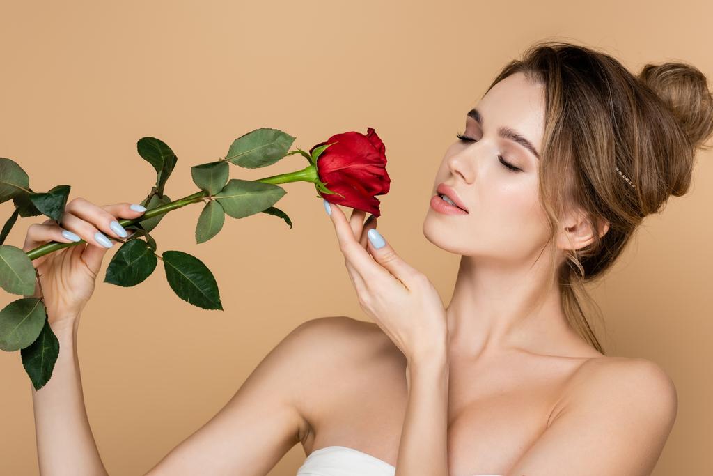 sensual woman with closed eyes and bare shoulders posing with red rose isolated on beige - Photo, Image