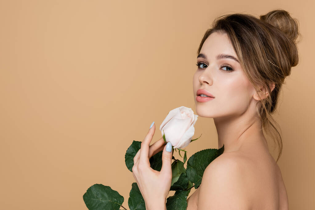 junge Frau mit natürlichem Make-up blickt in die Kamera nahe der weißen Rose isoliert auf Beige - Foto, Bild