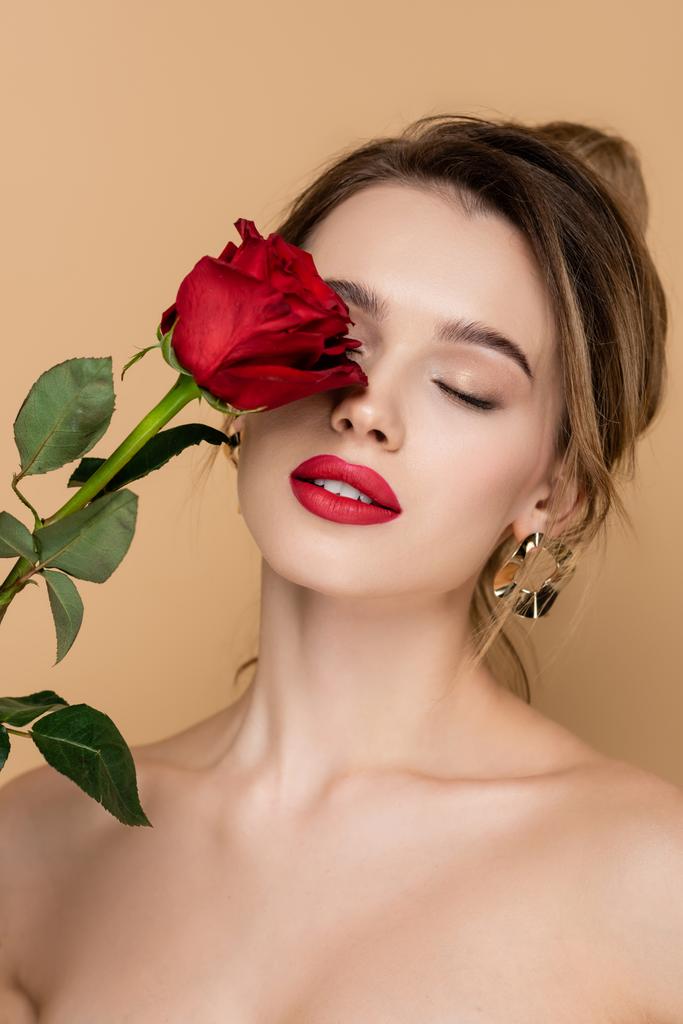 sinnliche Frau mit roten Lippen, die frische Rose in Gesichtsnähe hält, isoliert auf beige - Foto, Bild