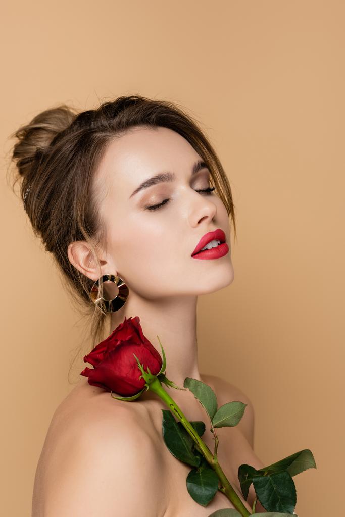 mulher sensual com ombros nus posando com os olhos fechados perto de rosa vermelha isolada no bege - Foto, Imagem