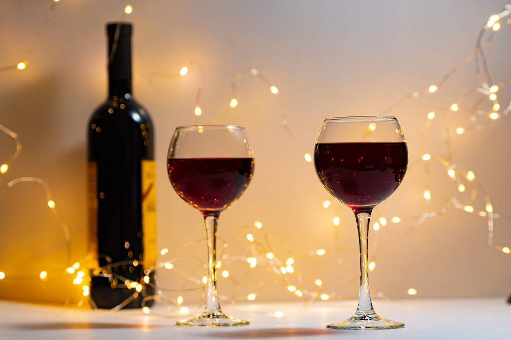 Photo horizontale de deux verres côte à côte de vin rouge et d'une bouteille de vin cher. Verres à vin avec vin rouge cher, bouteille, fond clair, romance, Saint Valentin, Noël, Nouvel An. - Photo, image