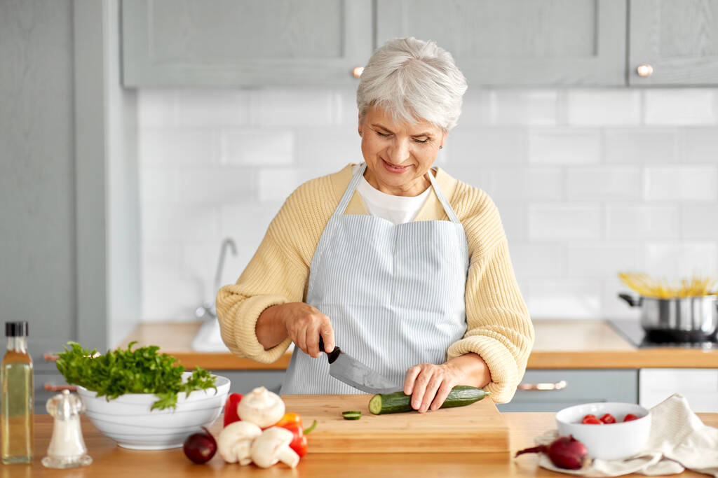счастливая женщина нарезает огурец на кухне - Фото, изображение