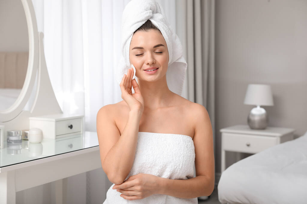 Piękna młoda kobieta z włosami owiniętymi w ręcznik czyszcząca twarz w domu - Zdjęcie, obraz