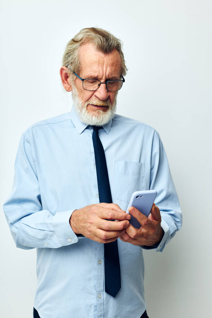 Porträt eines älteren Mannes im Hemd mit Krawatte, der auf hellem Hintergrund telefoniert - Foto, Bild