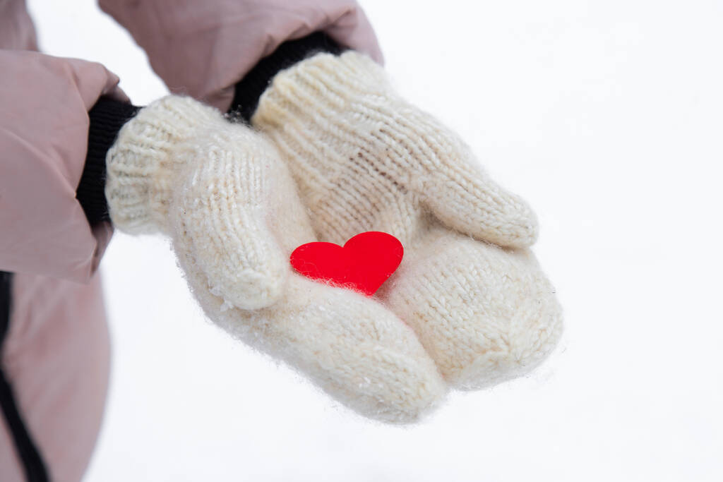 red heart lies on the fresh mittens. Winter snow. the woman dares in her palms a small red heart. Horizontal photo, close-up, top view. - Photo, Image