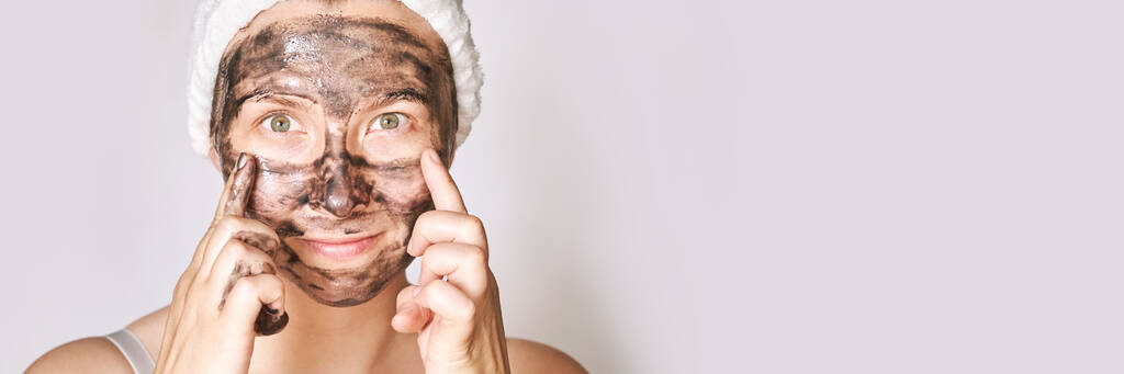 Junge Frau trägt schwarze Gesichtsmaske auf. Holzkohle Gesichtsbehandlung Produkt. Akne und Pickel - Foto, Bild