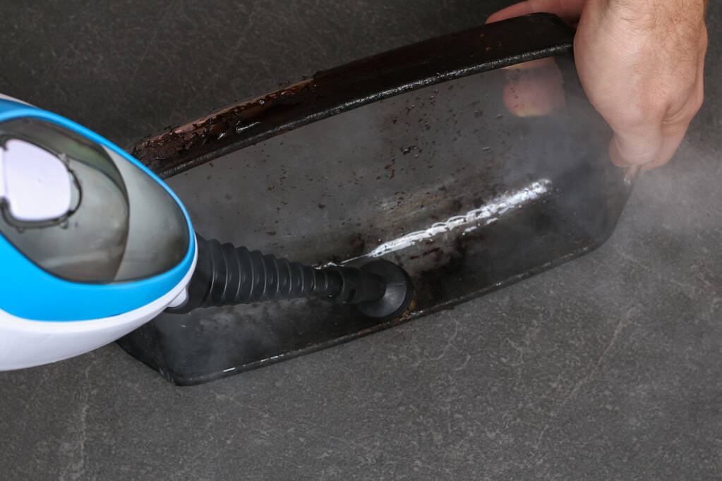 Mężczyzna czyści brudne naczynie do pieczenia grubą warstwą węgla specjalną dyszą do czyszczenia parowego - Zdjęcie, obraz