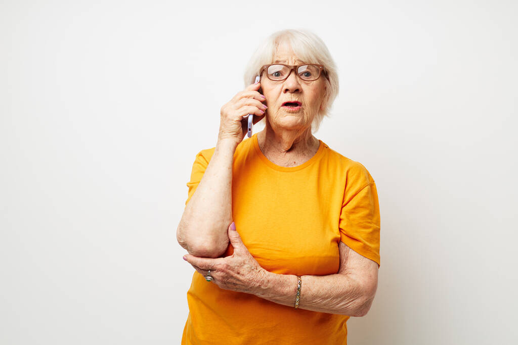 Portret starej, przyjaznej kobiety w żółtej koszulce pozowanie komunikacji przez telefon przycięty widok - Zdjęcie, obraz