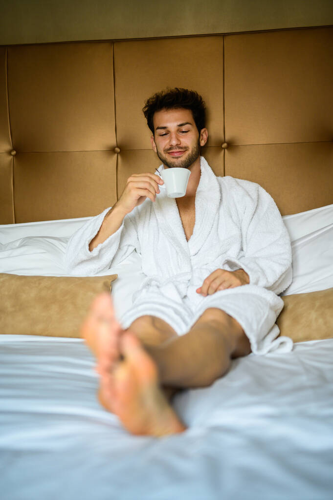 Genç ve yakışıklı adam sabahları bornozlu kahve içiyor. - Fotoğraf, Görsel