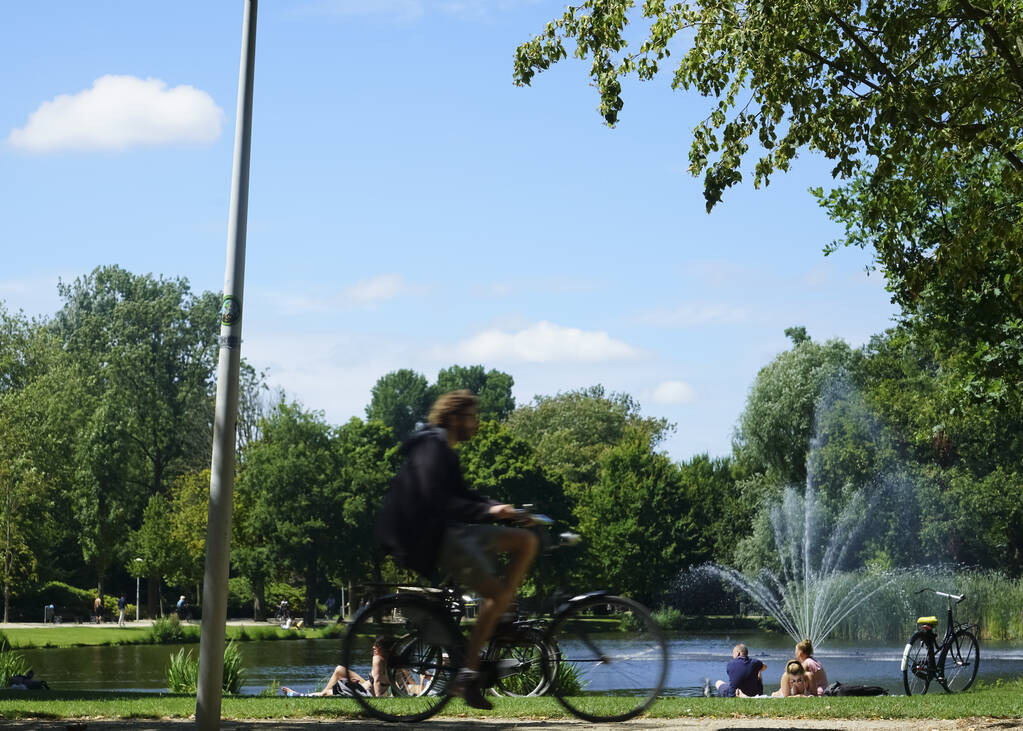 Amsterdam, Nederland - JULI 22, 2019: Vondelpark favoriete plek voor rust- en wandelaars en toeristen. silhouet van het rijden op fietsen man. - Foto, afbeelding