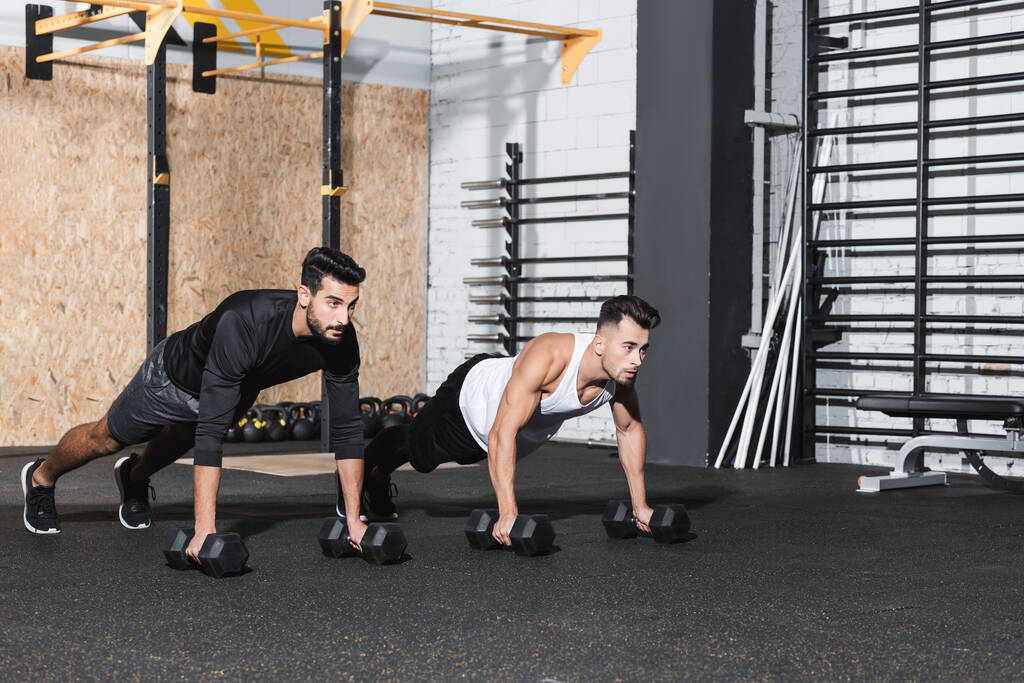 Young interracial sportsmen working out with dumbbells in gym  - Photo, Image
