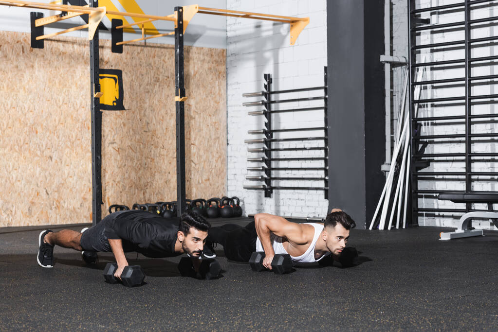 Multiethnic sportsmen doing press ups with dumbbells in gym  - Photo, Image