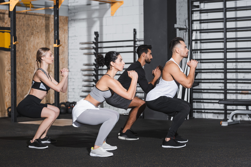 Seitenansicht multiethnischer Menschen bei Kniebeugen im Fitnessstudio  - Foto, Bild